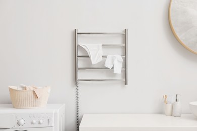 Photo of Heated towel rail with underwear and socks on white wall in bathroom