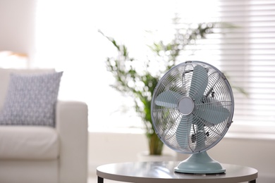 Photo of Modern electric fan on white table in living room. Space for text