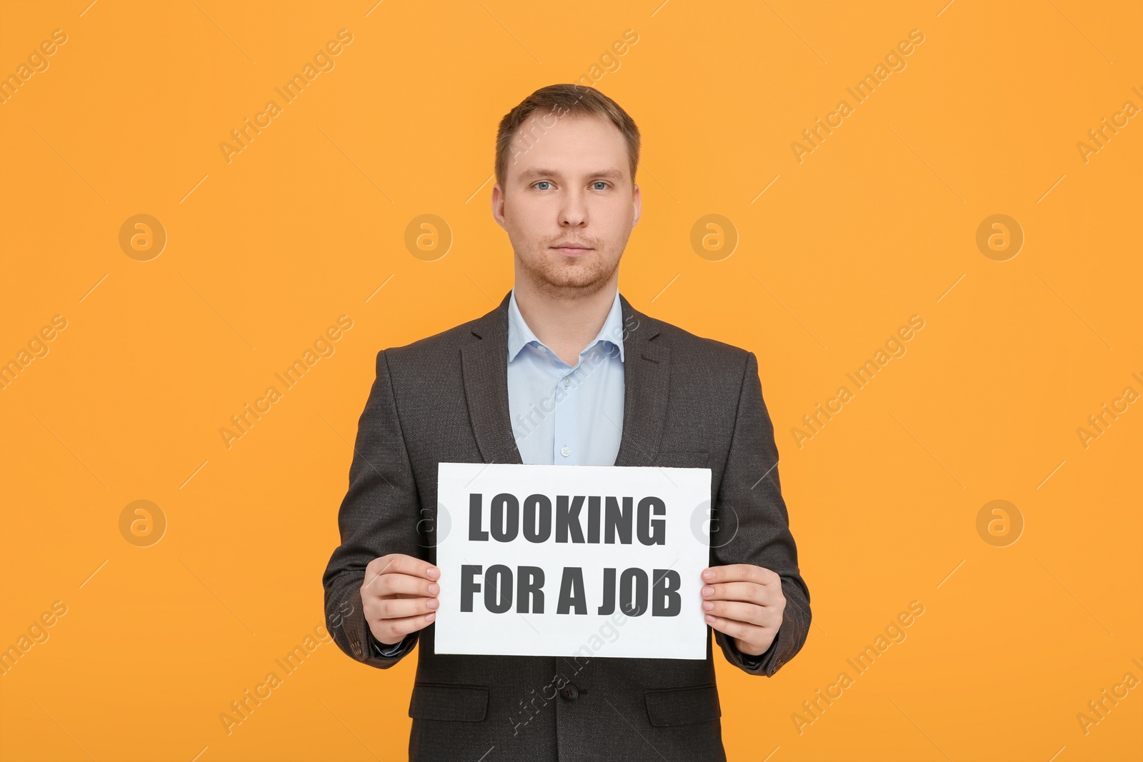 Photo of Unemployed man holding sign with phrase Looking For A Job on orange background