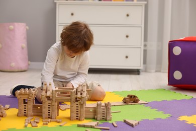 Photo of Little boy playing with wooden construction set on puzzle mat in room, space for text. Child's toy