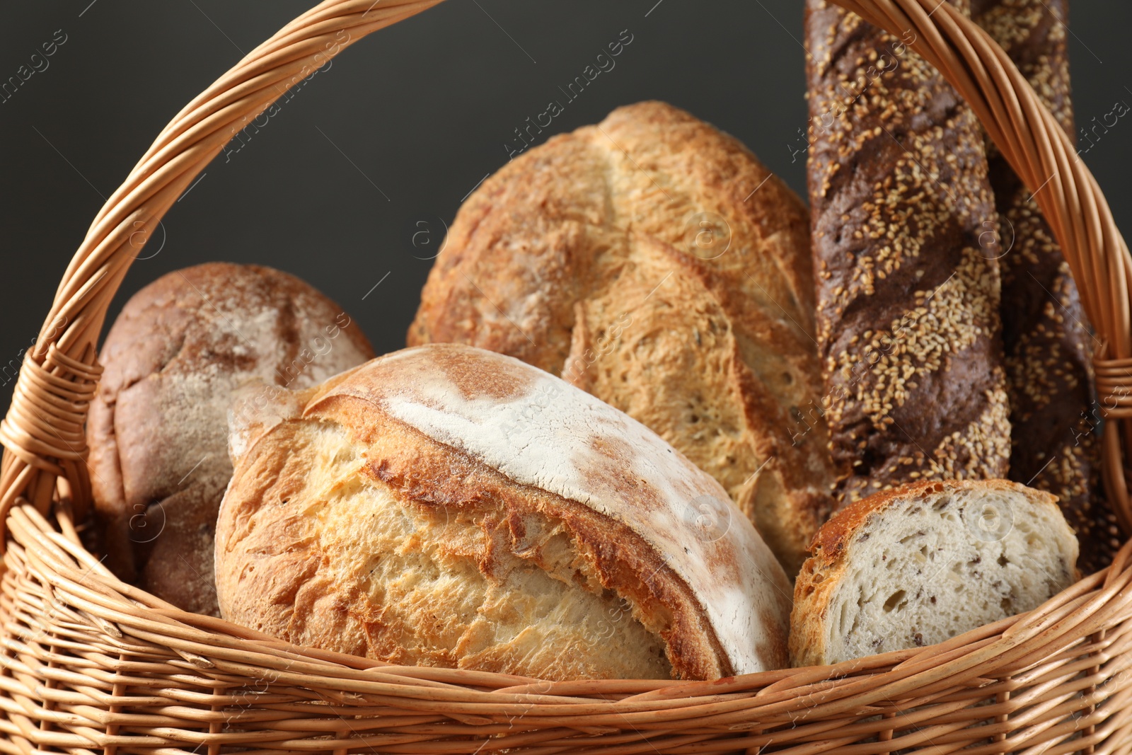 Photo of Wicker basket with different types of fresh bread against grey background, closeup