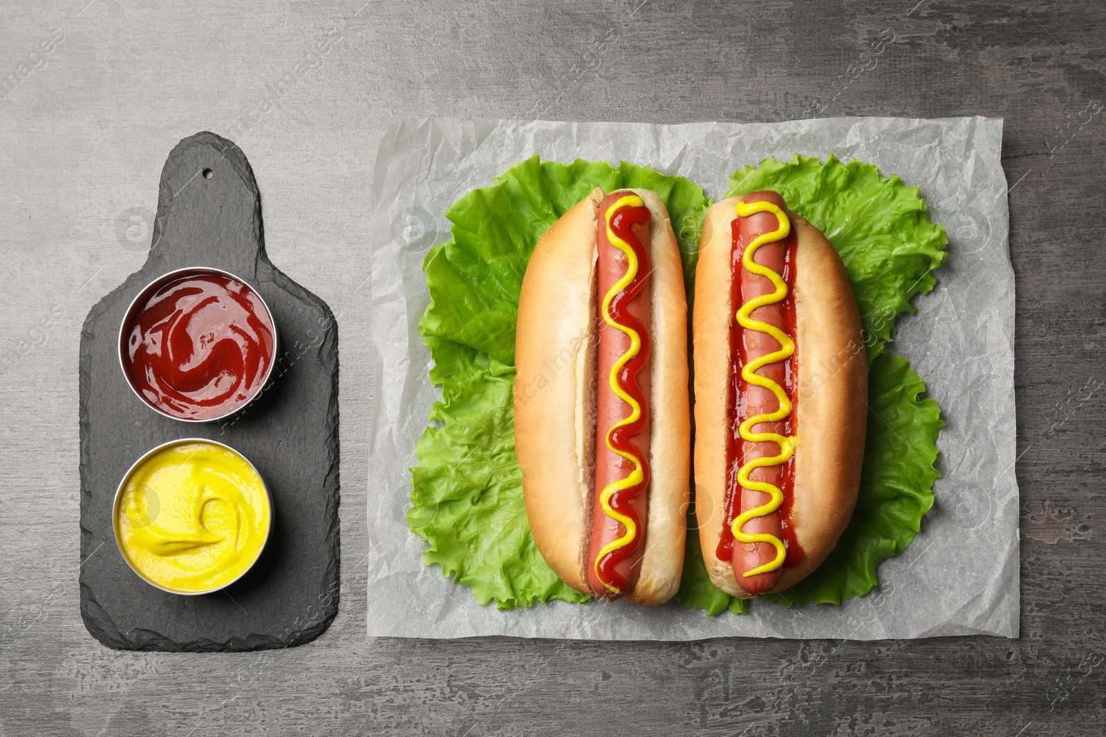 Photo of Delicious hot dogs with mustard, ketchup and lettuce on grey table, flat lay