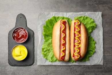 Photo of Delicious hot dogs with mustard, ketchup and lettuce on grey table, flat lay