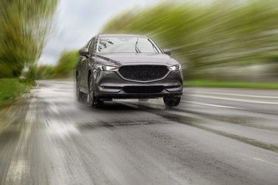 Black car driving at high speed on rainy day outdoors, motion blur effect