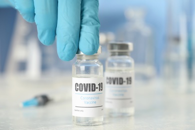 Photo of Doctor with coronavirus vaccine at table in laboratory, closeup