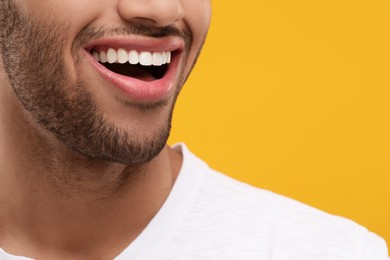 Smiling man with healthy clean teeth on orange background, closeup. Space for text