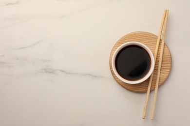 Bowl with soy sauce and chopsticks on white marble table, top view. Space for text