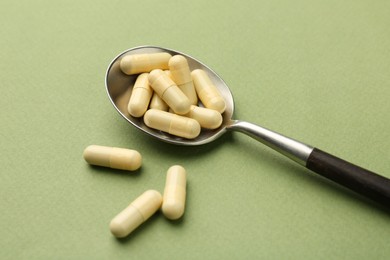 Vitamin capsules in spoon on olive background, closeup