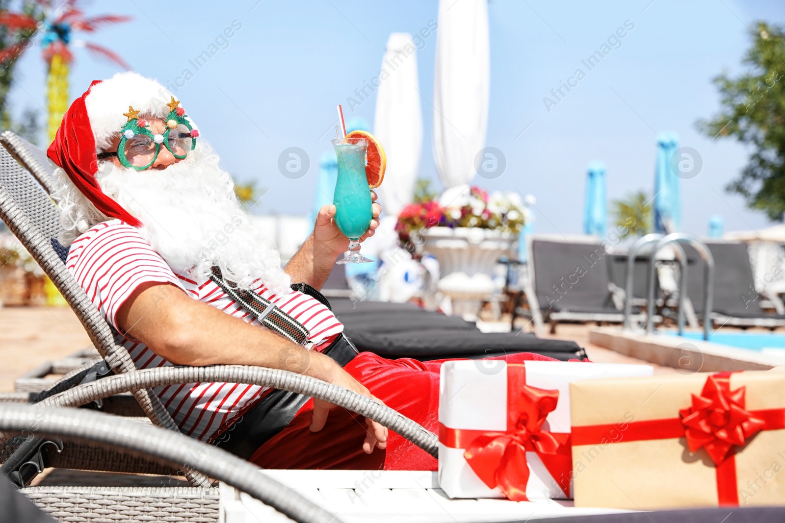 Photo of Authentic Santa Claus with cocktail resting on lounge chair at resort