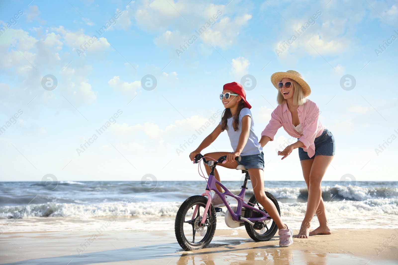 Photo of Happy mother teaching daughter to ride bicycle on sandy beach near sea