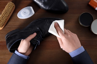 Photo of Man cleaning leather shoe at wooden table, top view