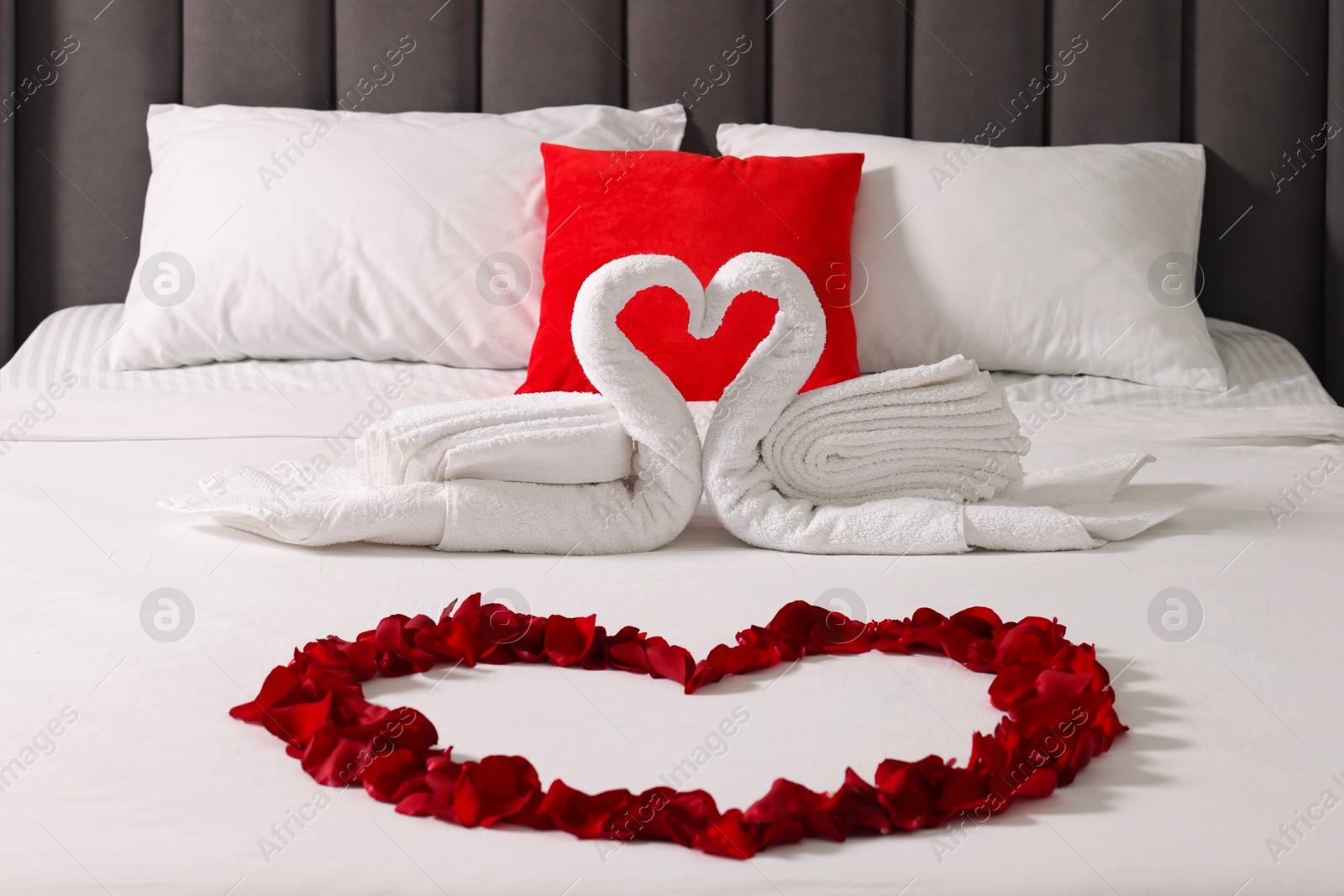 Photo of Honeymoon. Swans made with towels and heart of beautiful rose petals on bed in room