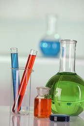 Photo of Laboratory analysis. Different glassware with liquids on white table against blurred background