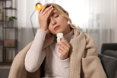 Sick woman wrapped in blanket with tissue at home. Cold symptoms