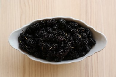 Bowl of delicious ripe black mulberries on wooden table, top view