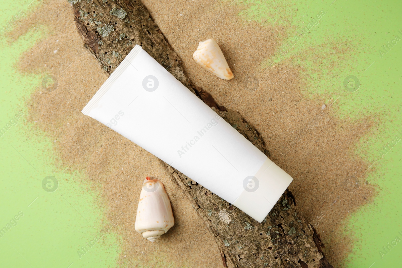 Photo of Flat lay composition with tube of cream and shells on sand against green background. Cosmetic product