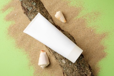 Photo of Flat lay composition with tube of cream and shells on sand against green background. Cosmetic product