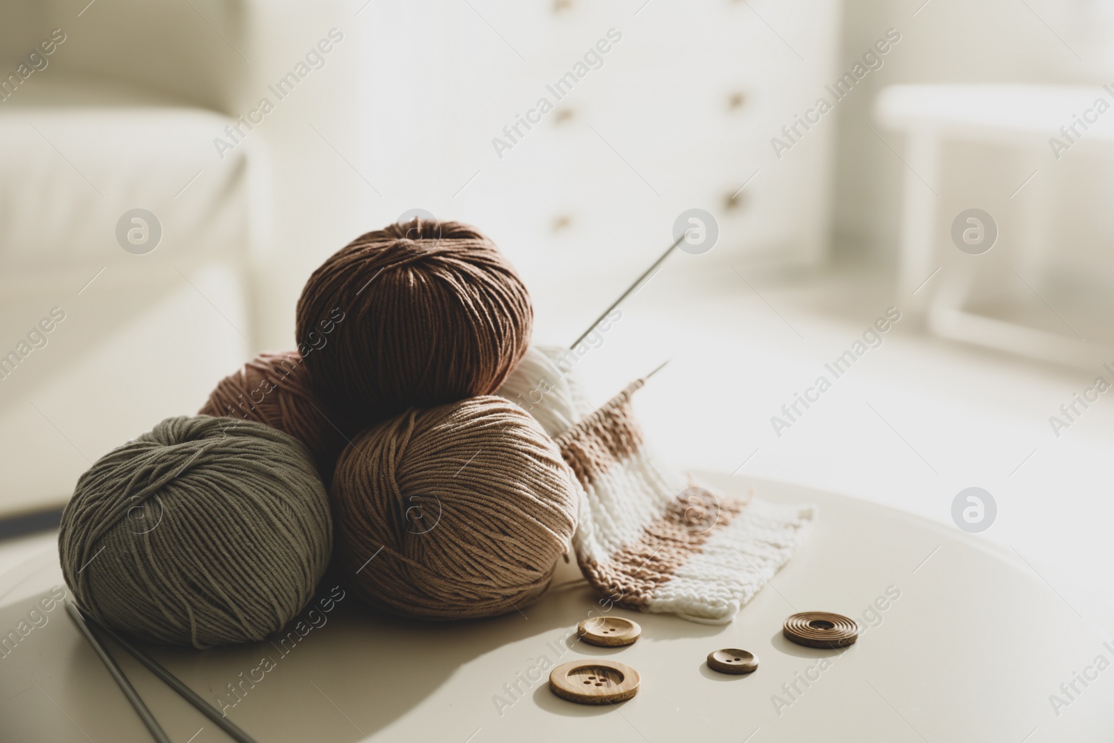 Photo of Yarn balls, buttons and knitting needles on white table indoors, space for text. Creative hobby