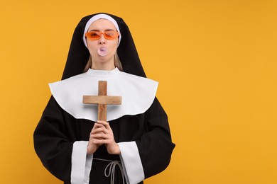 Photo of Woman in nun habit blowing bubble gum against orange background. Space for text