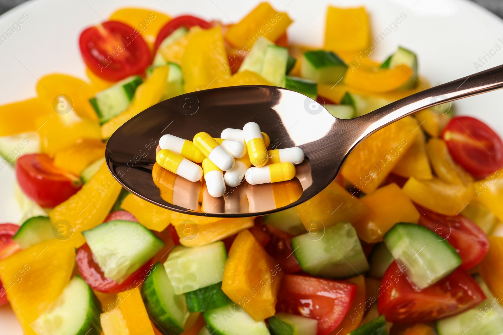 Photo of Spoon with weight loss pills over plate with vegetable salad, closeup