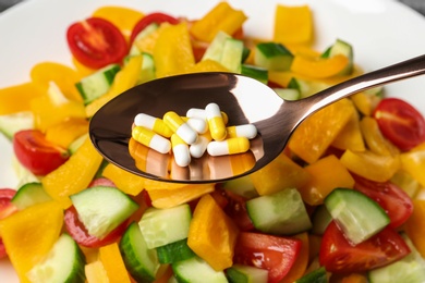 Photo of Spoon with weight loss pills over plate with vegetable salad, closeup