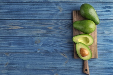 Photo of Board with ripe avocados on wooden background, top view