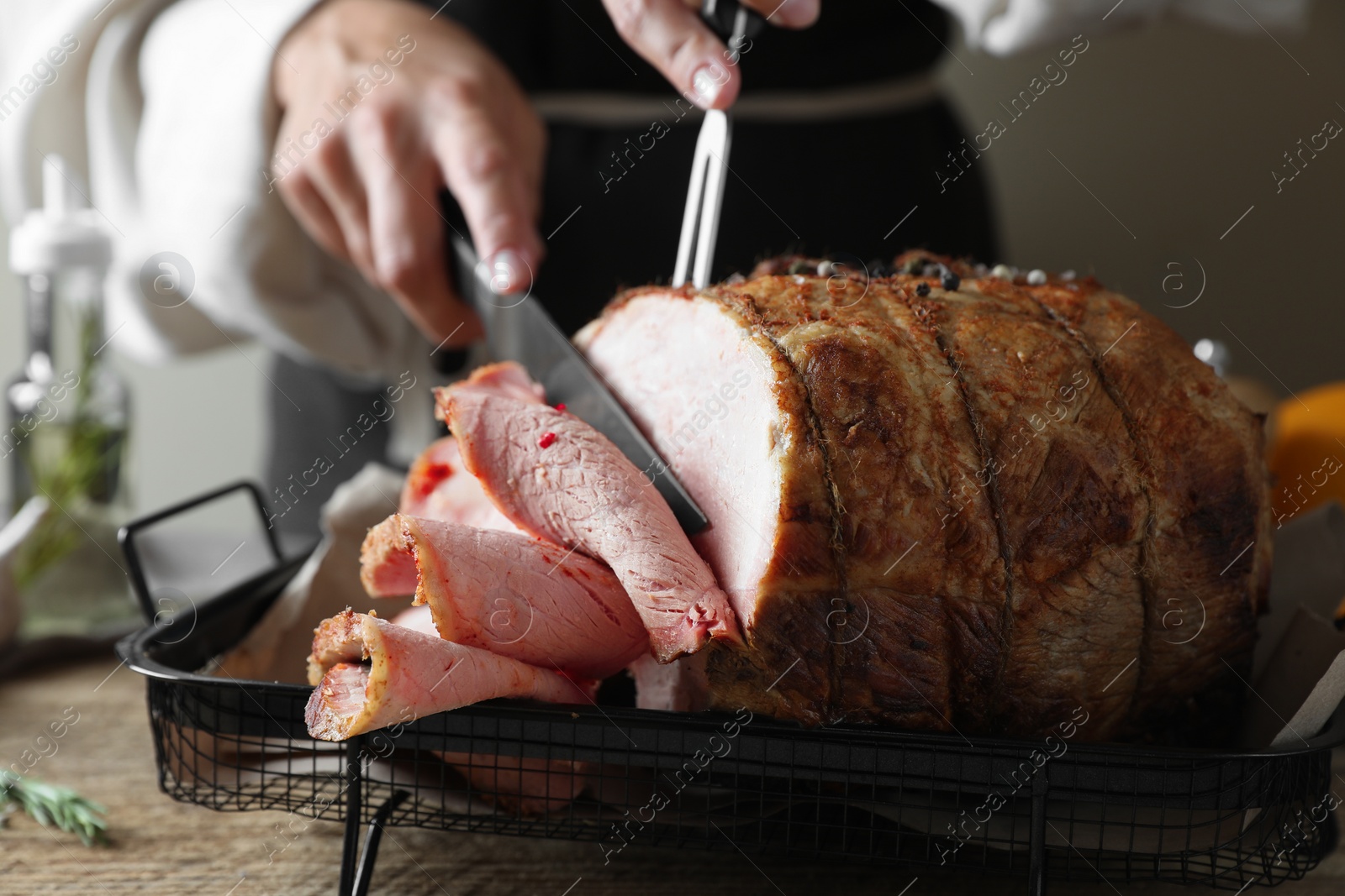 Photo of Woman cutting delicious baked ham at wooden table, closeup