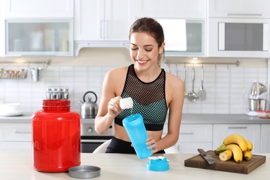 Photo of Young woman preparing protein shake at table in kitchen