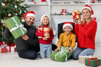 Photo of Happy family in Santa hats with Christmas gifts at home