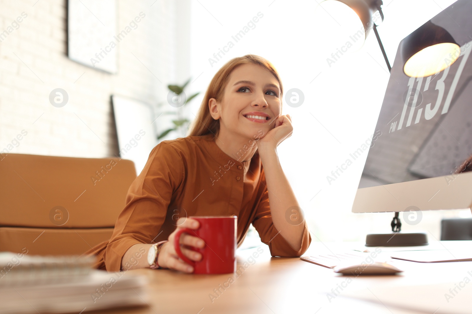 Photo of Young woman with cup of drink relaxing at table in office during break