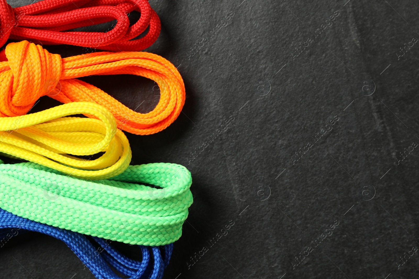 Photo of Colorful shoelaces on black background, flat lay. Space for text