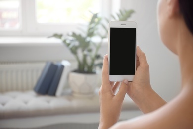 Photo of Young woman holding mobile phone with blank screen in hands indoors