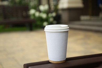 Paper cup of coffee on wooden bench outdoors. Takeaway drink