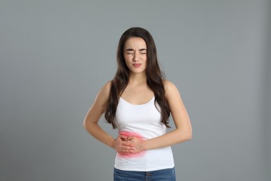 Young woman suffering from liver pain on grey background