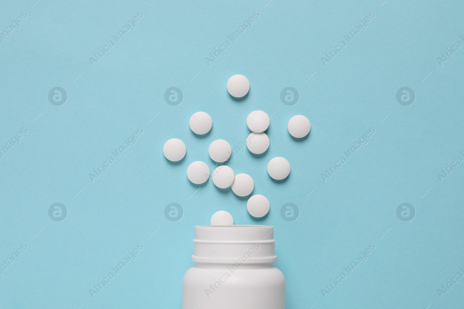 Photo of Plastic bottle with many white pills on light blue background, flat lay