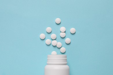 Photo of Plastic bottle with many white pills on light blue background, flat lay