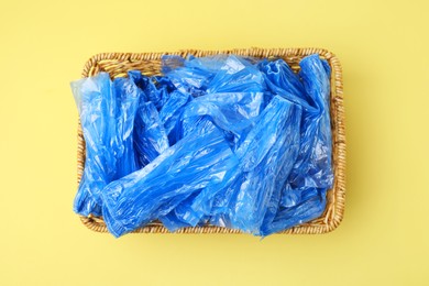 Photo of Blue medical shoe covers in wicker basket on yellow background, top view