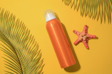Photo of Sunscreen, starfish and tropical leaves on yellow background, flat lay. Sun protection care