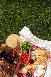 Photo of Picnic blanket with different products on green grass, top view. Space for text