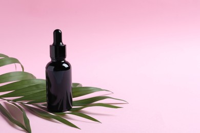 Bottle with cosmetic oil and green leaf on pink background. Space for text