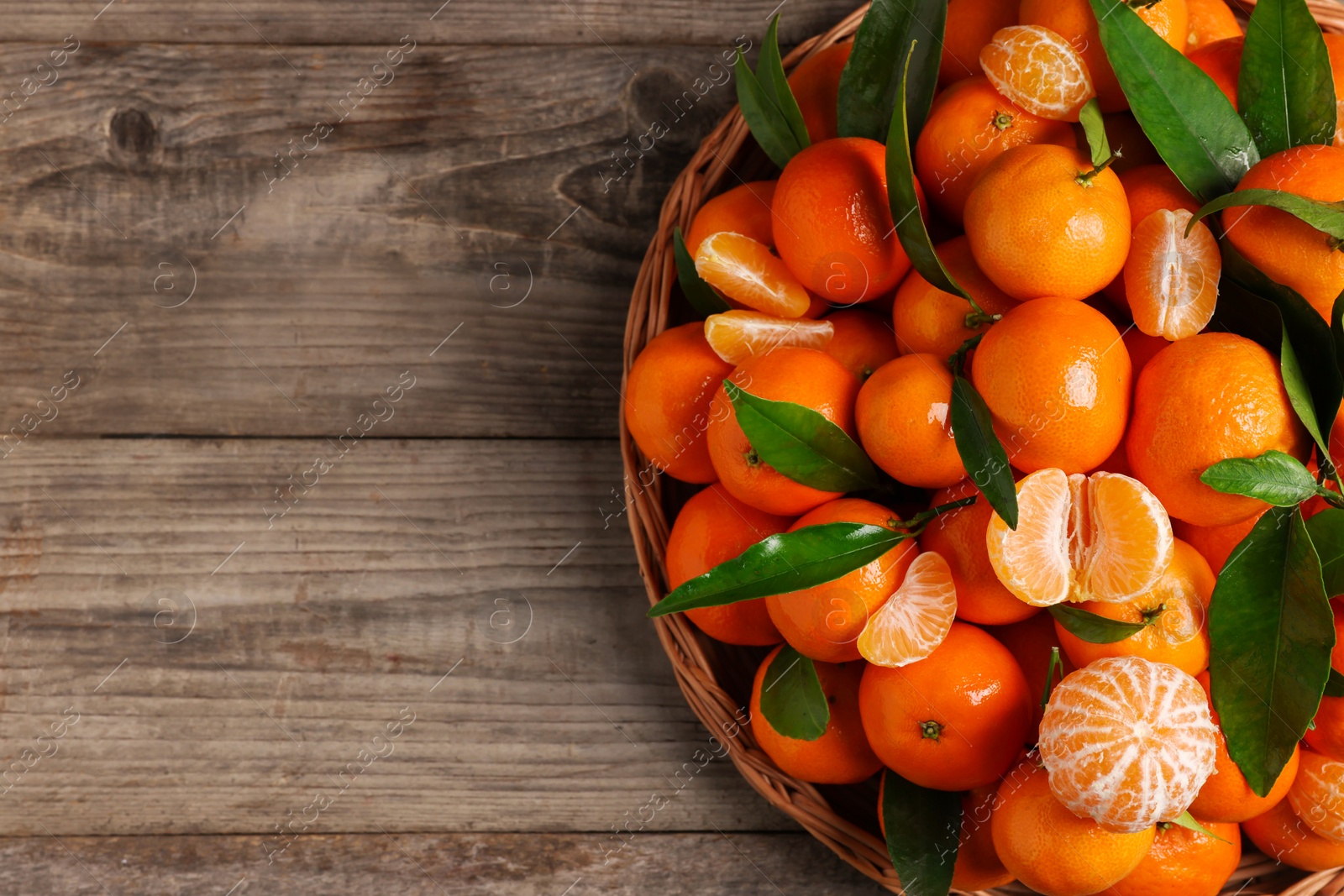 Photo of Fresh ripe juicy tangerines and green leaves on wooden table, top view. Space for text