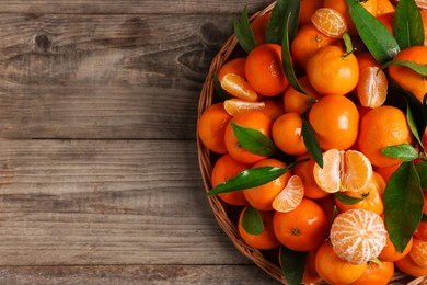 Fresh ripe juicy tangerines and green leaves on wooden table, top view. Space for text