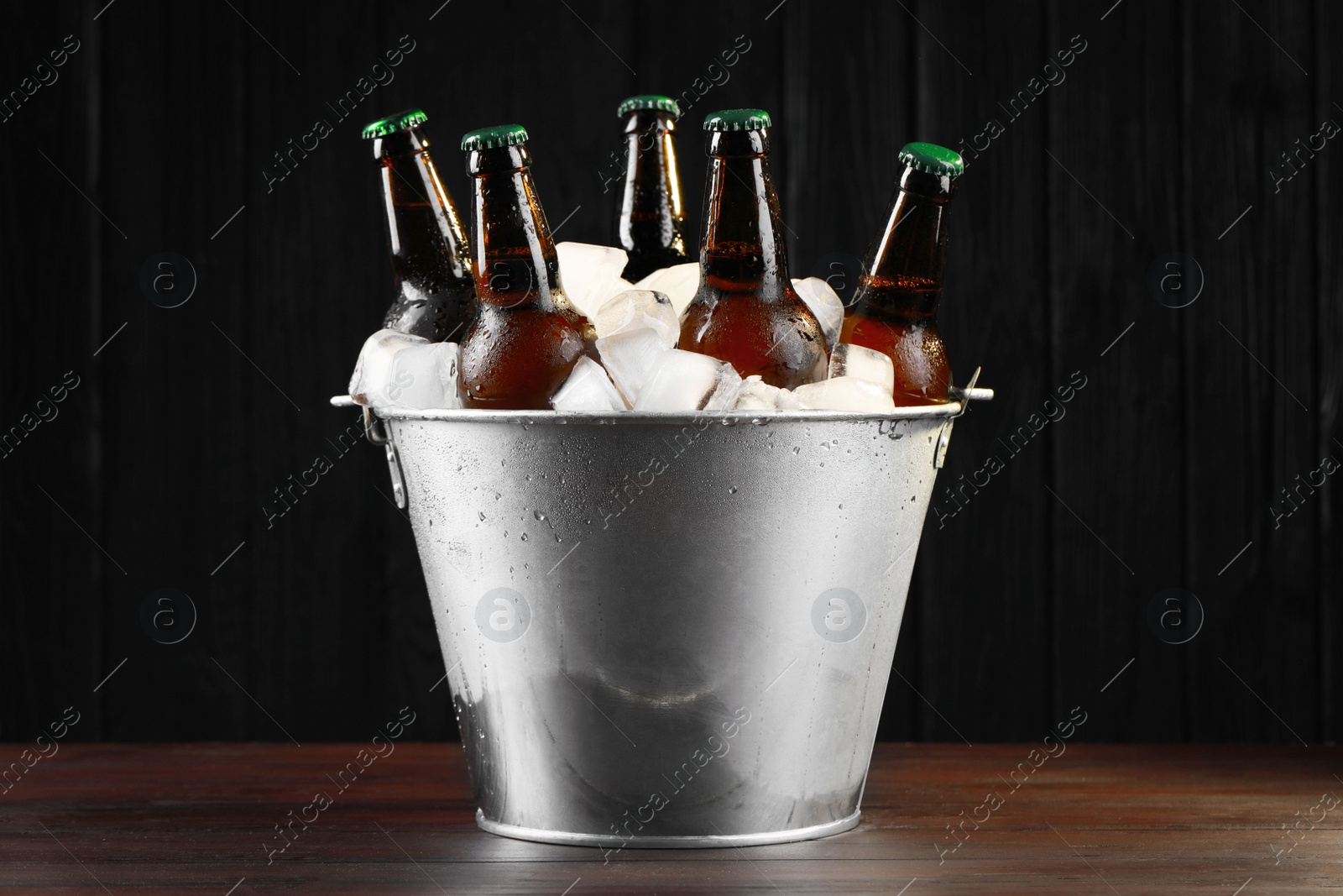 Photo of Metal bucket with bottles of beer and ice cubes on wooden table