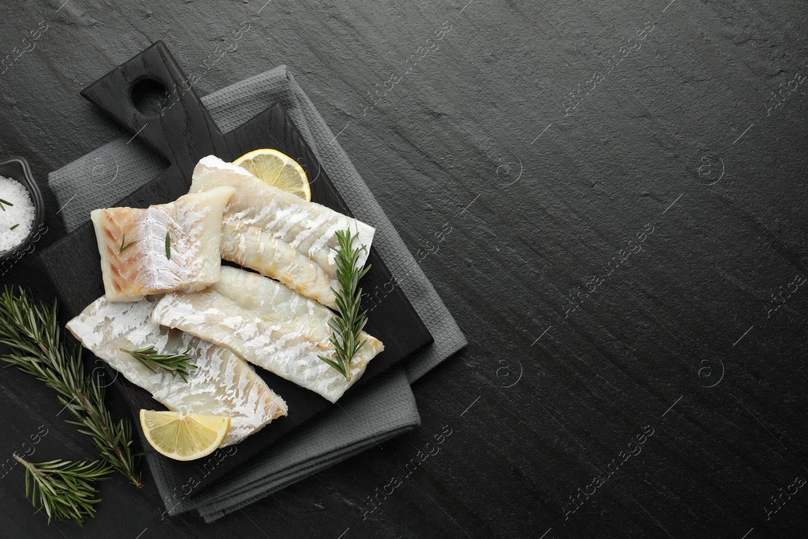 Photo of Fresh raw cod fillets, rosemary, lemon and salt on black table, flat lay. Space for text