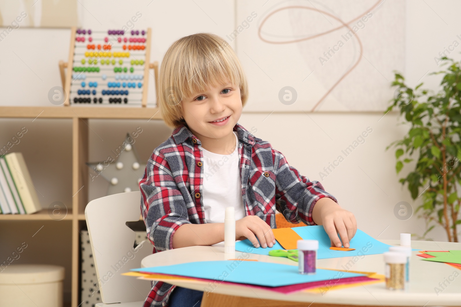 Photo of Cute little boy with colorful paper at desk in room. Home workplace