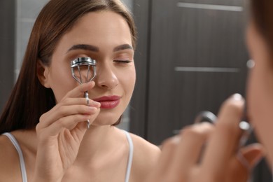 Woman using eyelash curler near mirror indoors