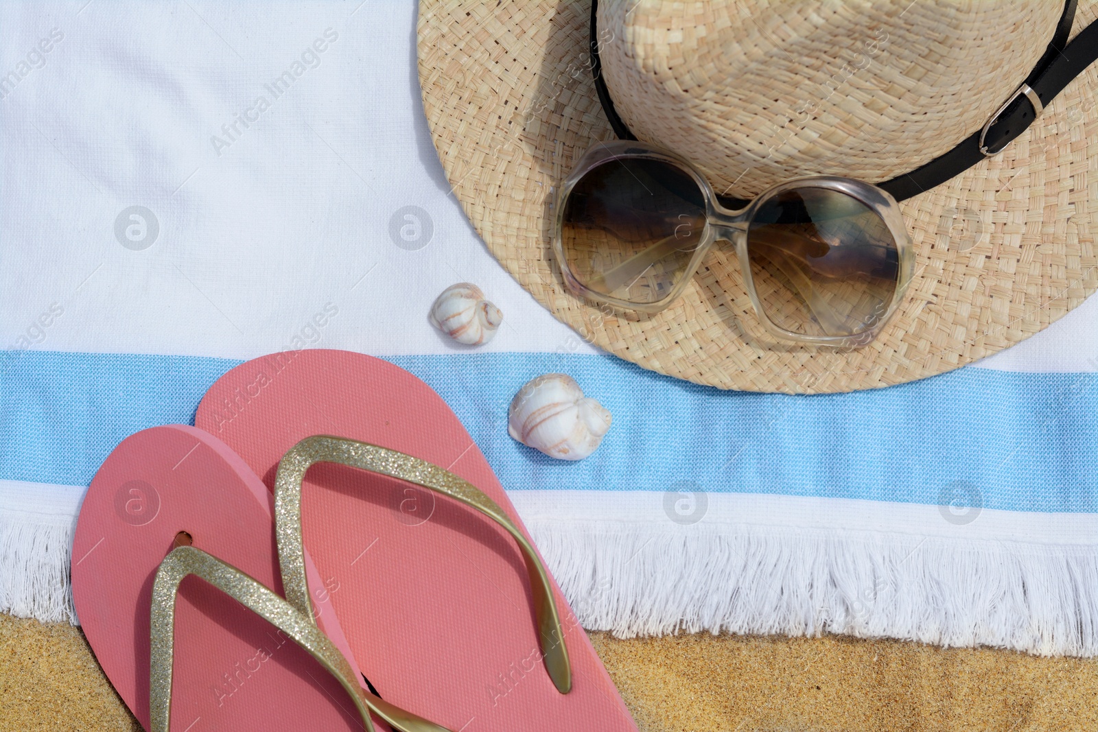 Photo of Beach towel with straw hat, seashells, sunglasses and flip flops on sand, flat lay