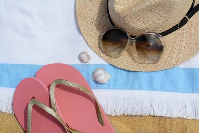 Photo of Beach towel with straw hat, seashells, sunglasses and flip flops on sand, flat lay