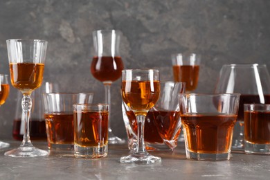 Photo of Different delicious liqueurs in glasses on grey table