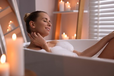 Beautiful woman taking bath in tub with foam indoors. Romantic atmosphere